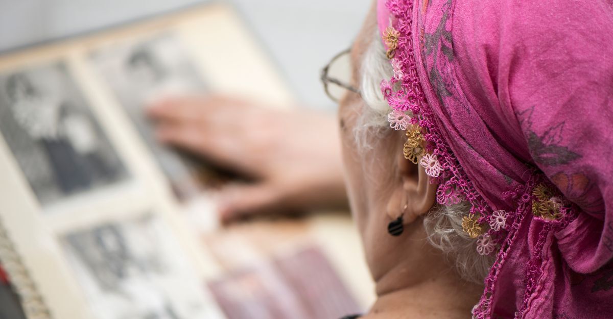 Donna anziana con foulard rosa sfoglia un vecchio album di foto