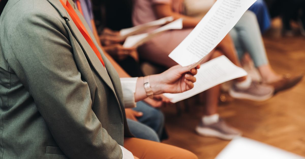 Prova del coro, lezione di canto nella sala dell'auditorium, gruppo sul palco tengono in mano dei fogli e cantano. Lezione di canto d'orchestra in una scuola di musica con un insegnante, adulti cantano in coro.
