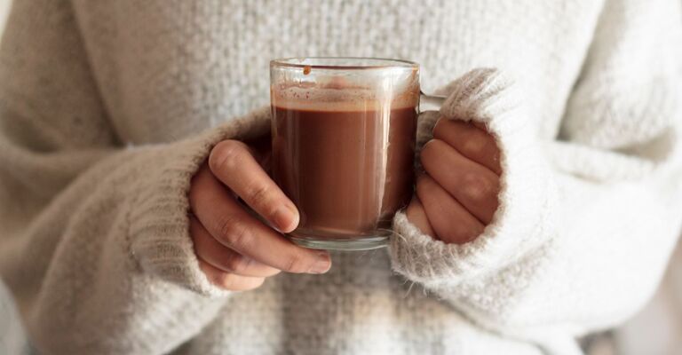 Donna in maglione bianco che tiene una tazza di cioccolata calda