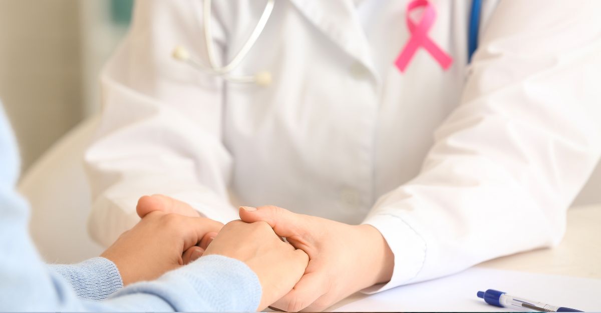 Primo piano di un medico con un nastro rosa sulla camicia bianca che stringe con empatia le mani di un paziente