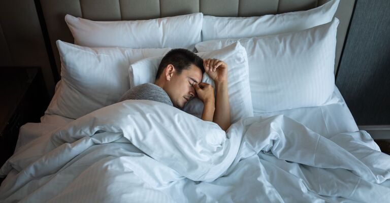 L'uomo esausto non riesce a dormire. Si tiene la testa tra le mani mentre è sdraiato nel letto.