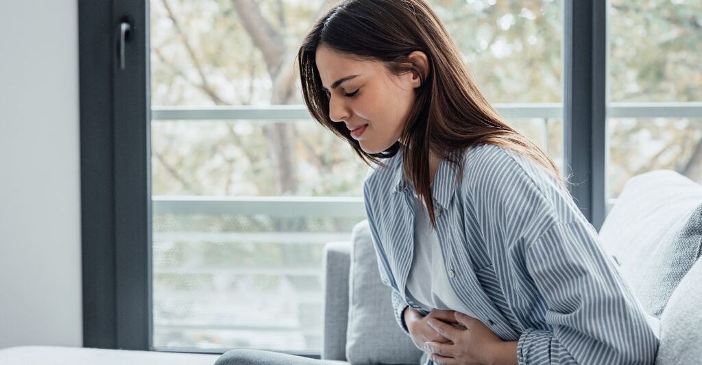 Giovane donna malata che soffre di dolori, si tiene la pancia, ha la sensazione di avere male allo stomaco, ha dolori addominali, sintomi di gastrite, pancreatite o diarrea.