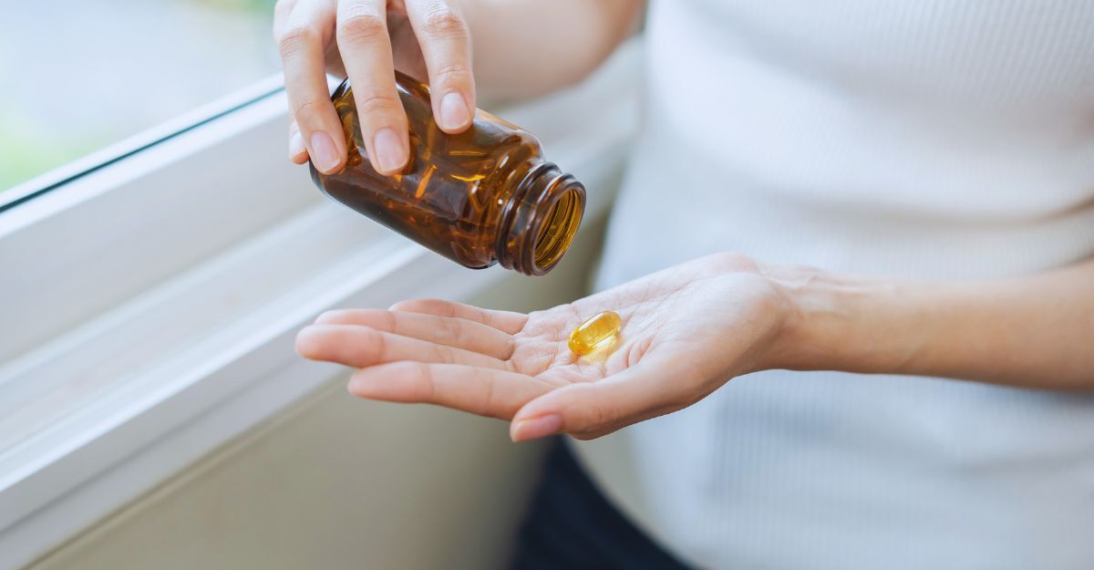 Primo piano di giovane donna che tiene in mano compresse o capsule dalla bottiglia di medicinali, trattamento vitaminico assunto a casa