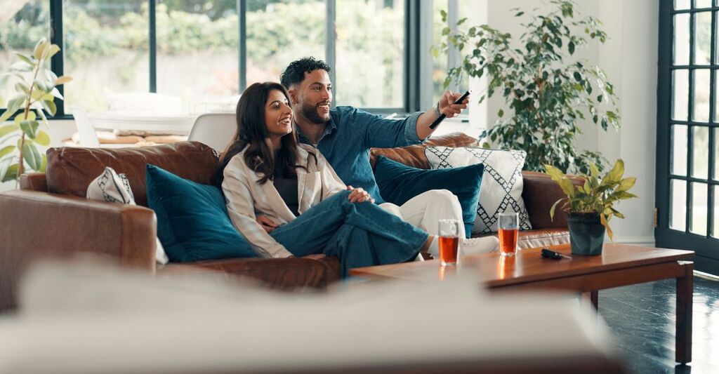 Coppia di uomo e donna che guarda insieme la tv sul divano mentre sorridono insieme. Soggiorno di una casa moderna
