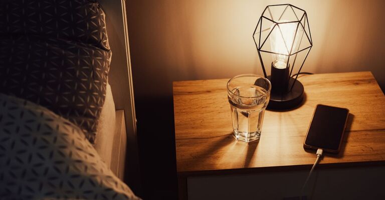 Lampada da notte retrò vicino al letto. Luce soffusa nella stanza. Illuminazione con lanterna. Una sana routine del sonno notturno con dispositivi elettronici spenti e acqua per idratarsi.