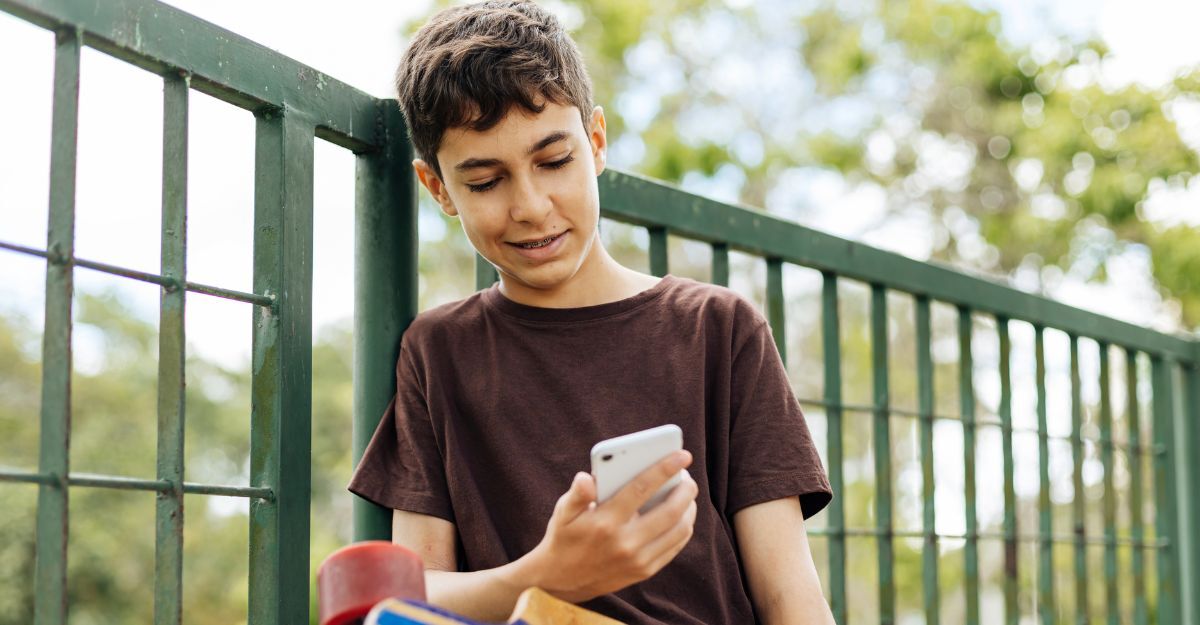 Un bambino appoggiato ad una ringhiera con in mano un cellulare