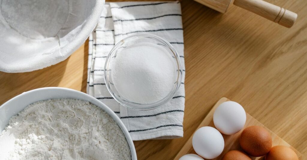 Primo piano di uova, farina e soprattutto una ciotola con lo zucchero su un tavolo per fare un dolce
