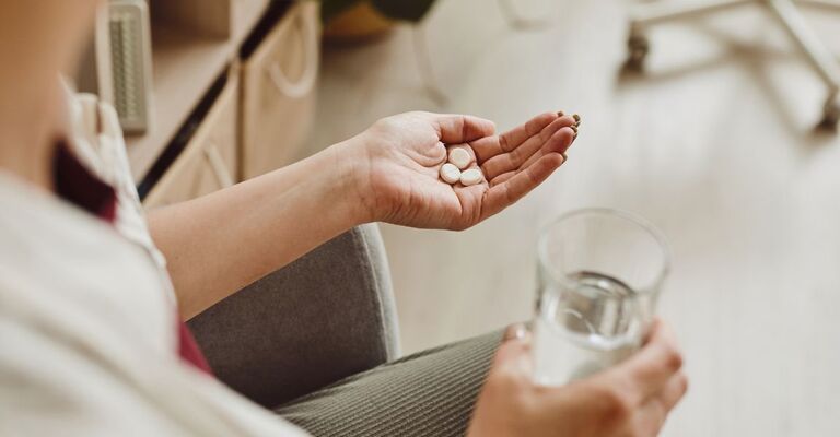 Primo piano dall'alto di una donna irriconoscibile che tiene in mano pillole e un bicchiere d'acqua, medicina e trattamento di recupero