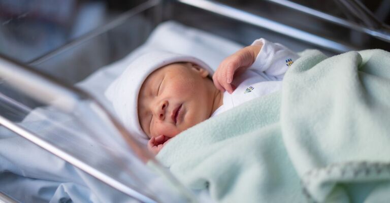 Ritratto ravvicinato di un'adorabile neonata sdraiata tranquilla nella culla dell'ospedale poche ore dopo essere venuta alla luce