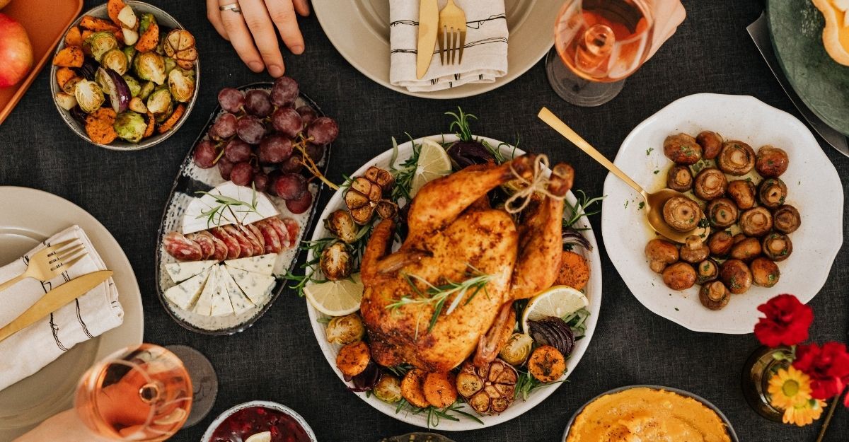 Una tavola imbandita vista dall'alto con pollo arrosto, verdure grigliate, uva, formaggi e bicchieri di vino