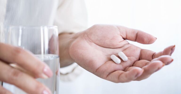 Primo piano della mano di una donna che prende una pillola probiotica per il trattamento della diarrea, problema all'apparato digerente