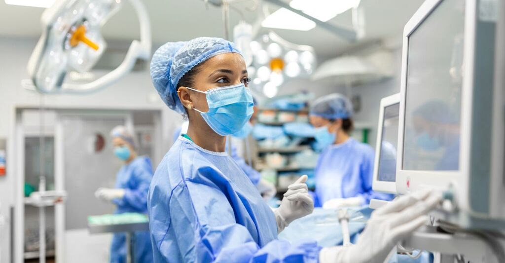 Anestesista che lavora in sala operatoria indossando dispositivi di protezione mentre controlla i monitor mentre seda il paziente prima di un intervento chirurgico in ospedale
