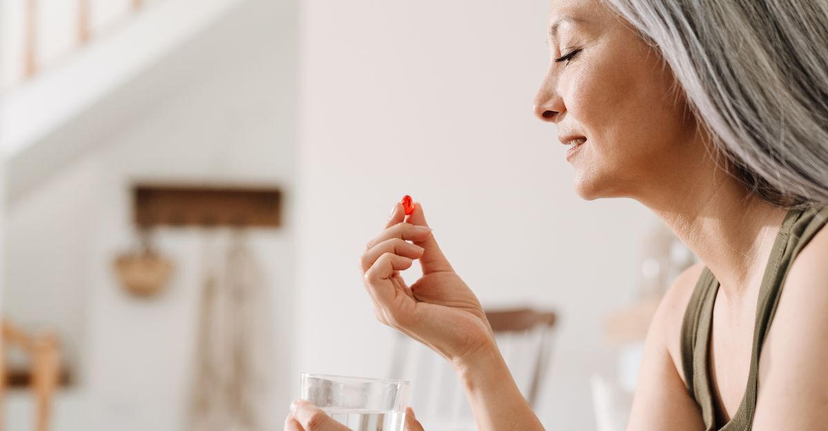 Donna matura che prende le sue medicine mentre è seduta sul divano con un bicchiere di acqua