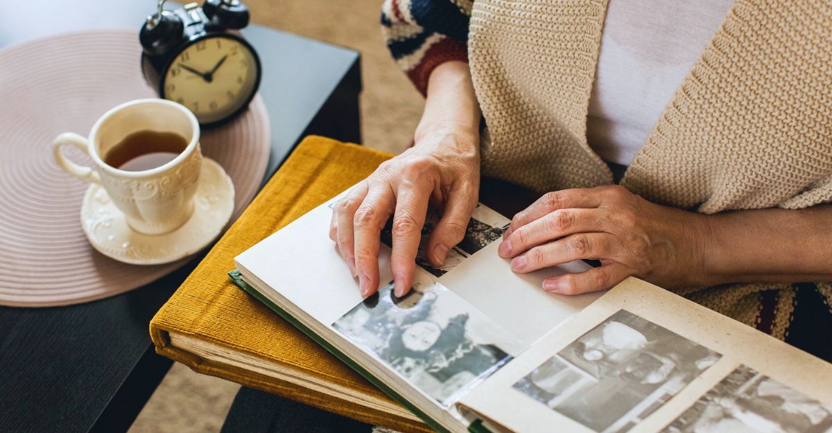 Mani di una donna anziana che guarda l'album fotografico con accanto una tazzina di caffè e una sveglia