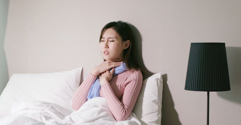 Una donna con mal di gola ricorrente a letto in camera.