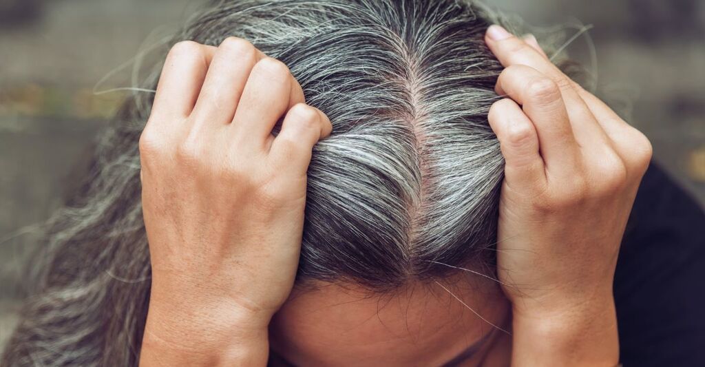 Donna con capelli grigi alle radici e viso preoccupato e stressato che guarda in basso