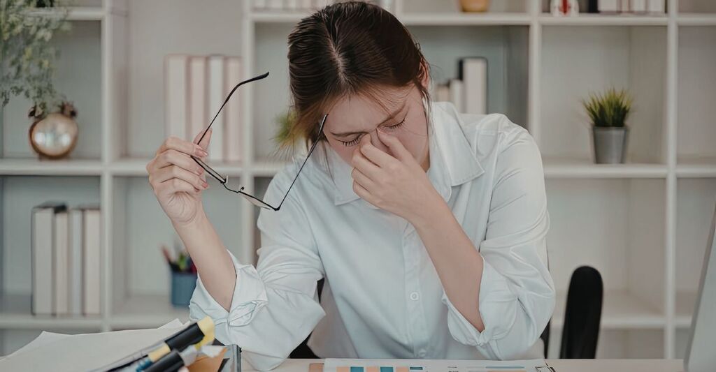 Donna alla scrivania che si toglie gli occhiali e si massaggia gli occhi, esausta per il lavoro d'ufficio