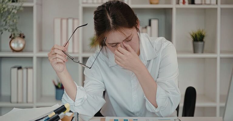 Donna alla scrivania che si toglie gli occhiali e si massaggia gli occhi, esausta per il lavoro d'ufficio