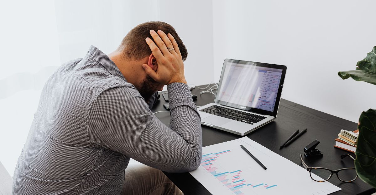 Uomo seduto alla scrivania che si tiene la testa con le mani in un momento di forte stress o stanchezza davanti al computer