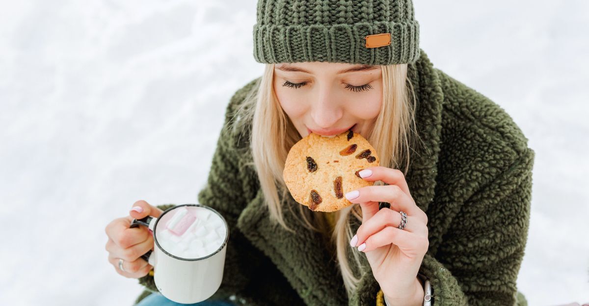 Una donna in inverno sulla neve mangia carboidrati da un biscotto.