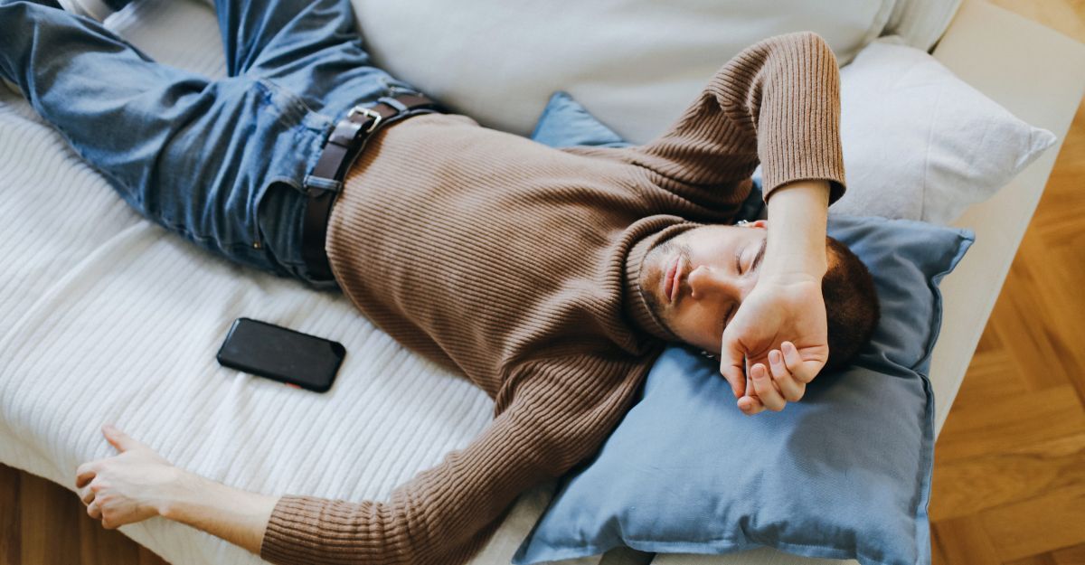 Un uomo riposa disteso su un divano con un braccio sugli occhi e uno smartphone accanto a sé