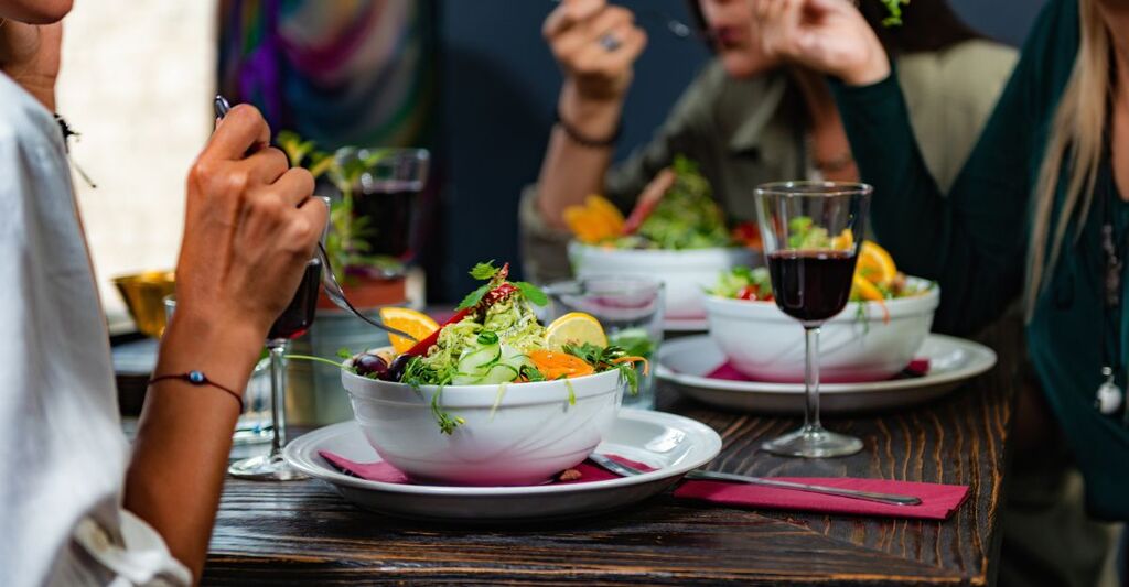 Persone a tavola che mangiano insalate gourmet colorate accompagnate da vino rosso