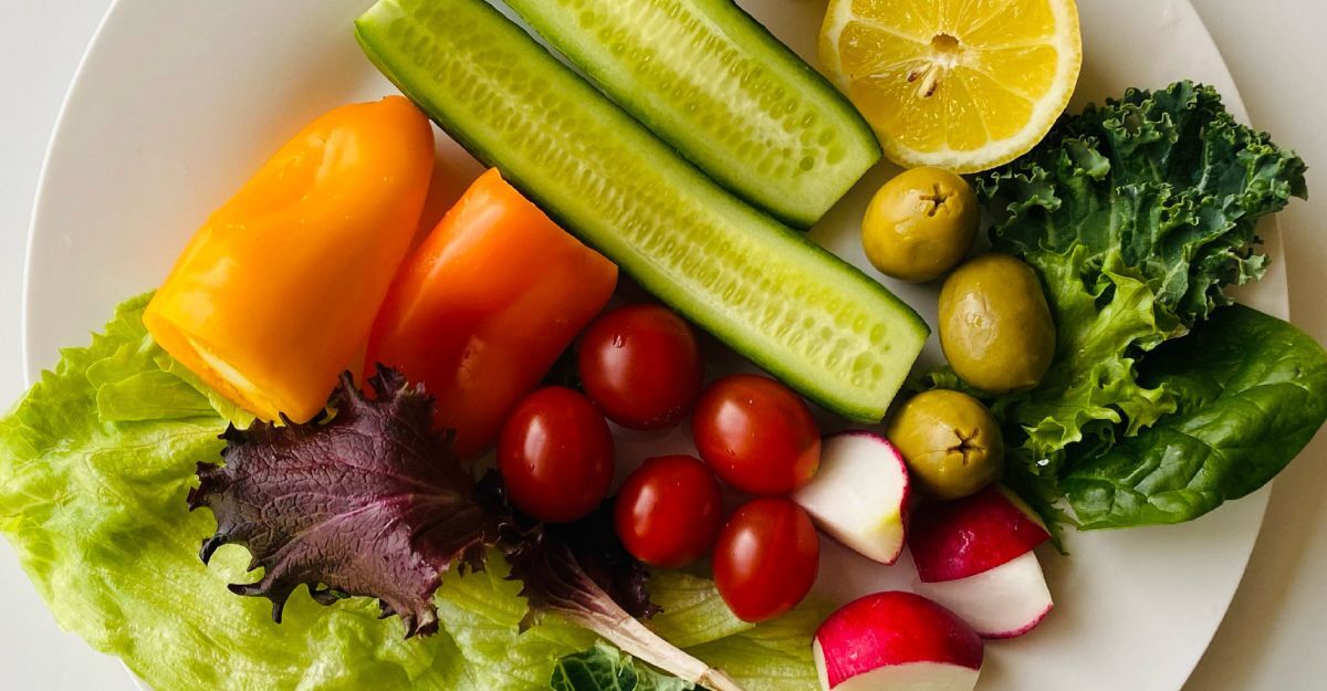 Piatto bianco con verdure fresche assortite: peperoni, cetrioli, pomodorini, ravanelli, olive, limone e foglie di insalata mista