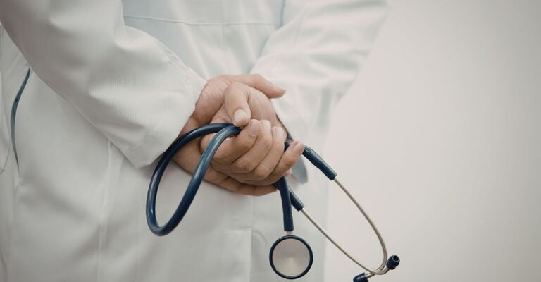 Primo piano delle mani di un medico in camice bianco che tiene uno stetoscopio dietro la schiena