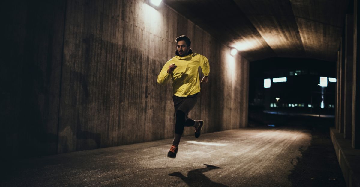 Un uomo con giacca gialla catarifrangente corre in un sottopassaggio illuminato di notte