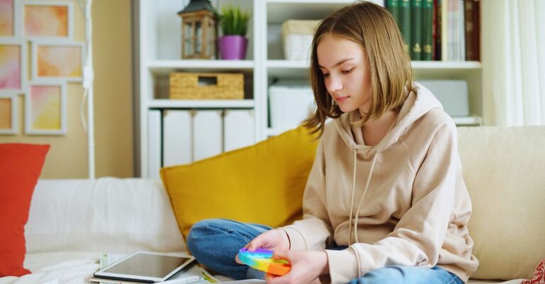 Una ragazzina gioca con un giocattolo pop-it arcobaleno mentre studia a casa. Un'adolescente con un gioco di tendenza per alleviare stress e ansia.