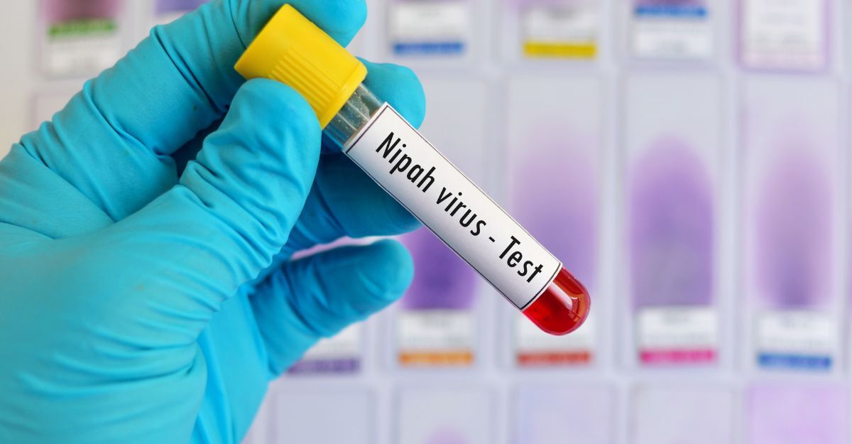 Una mano con guanto azzurro tiene una provetta di sangue con l'etichetta "Nipah virus - Test"