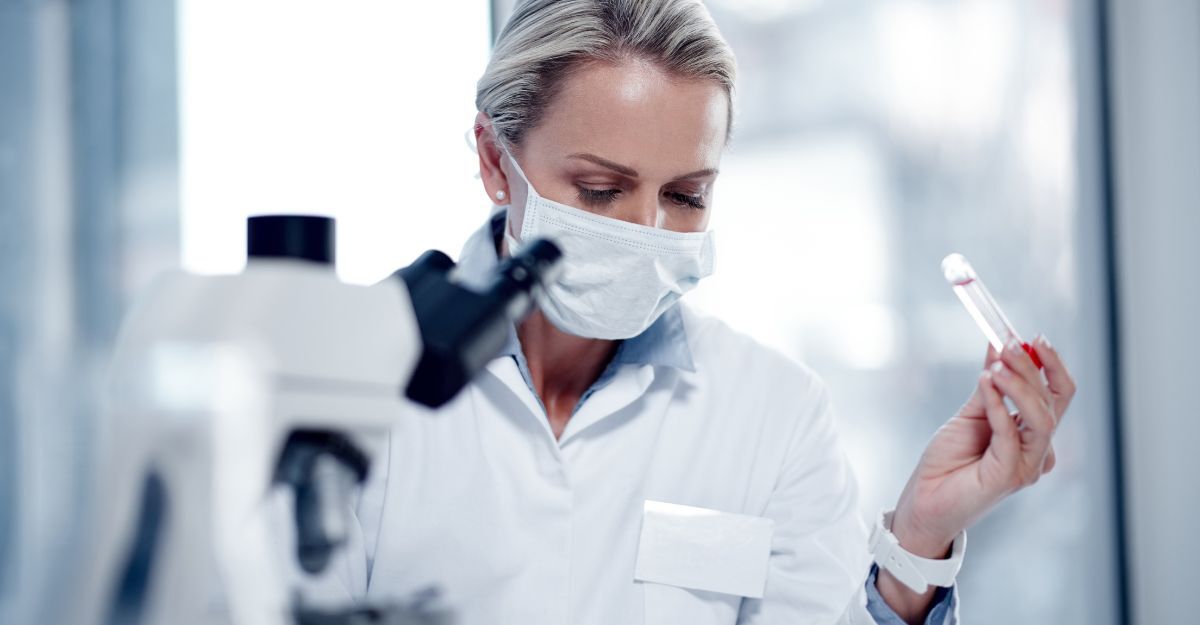 Un medico che studia al microscopio con una provetta di sangue in mano