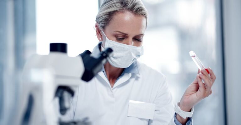 Un medico che studia al microscopio con una provetta di sangue in mano