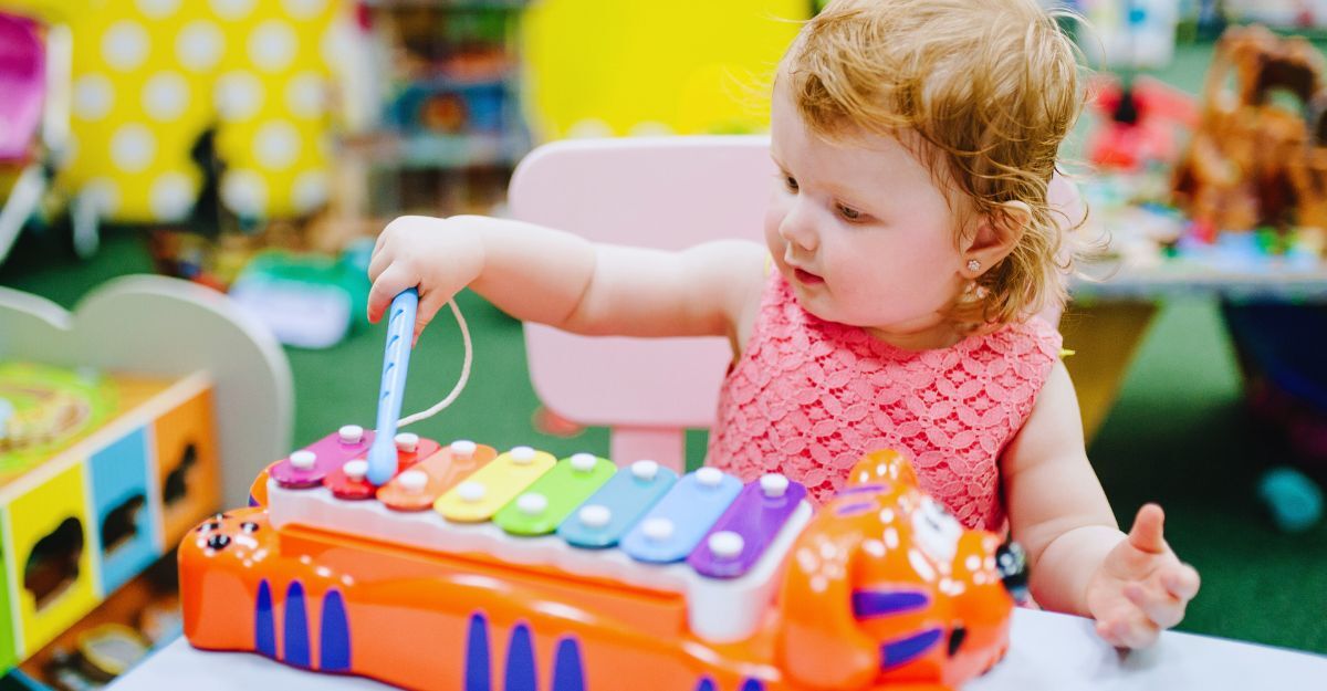Una bambina felice di 1 anno suona uno strumento musicale, lo xilofono, nella sala giochi della sua cameretta per il compleanno o a casa.