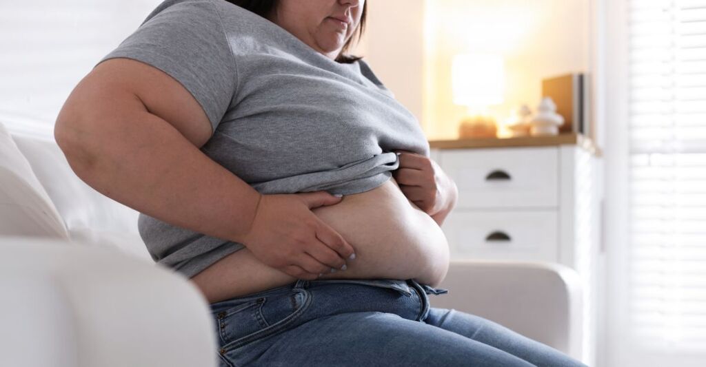 Una donna con obesità si guarda la pancia.