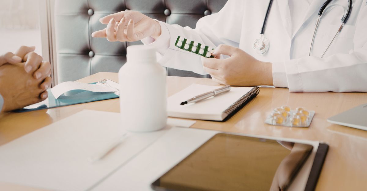 Un medico in camice bianco mostra un blister di pillole a un paziente seduto di fronte a lui durante una visita