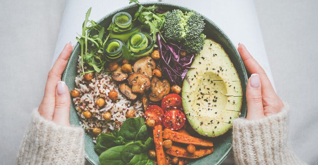 Donna che tiene in mano un piatto con cibo vegano o vegetariano. Dieta sana a base vegetale. Cena o pranzo sano. Ciotola Buddha con verdure fresche. Alimentazione sana.