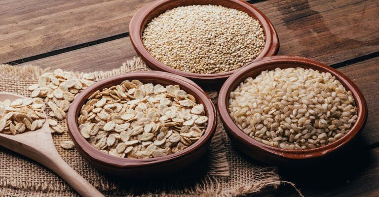 Tre ciotole di terracotta contenenti fiocchi d'avena, quinoa e riso integrale su un tavolo di legno