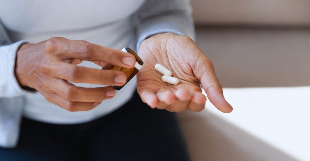 Ragazza nera tiene in mano delle pillole bianche e un barattolo. Primo piano.