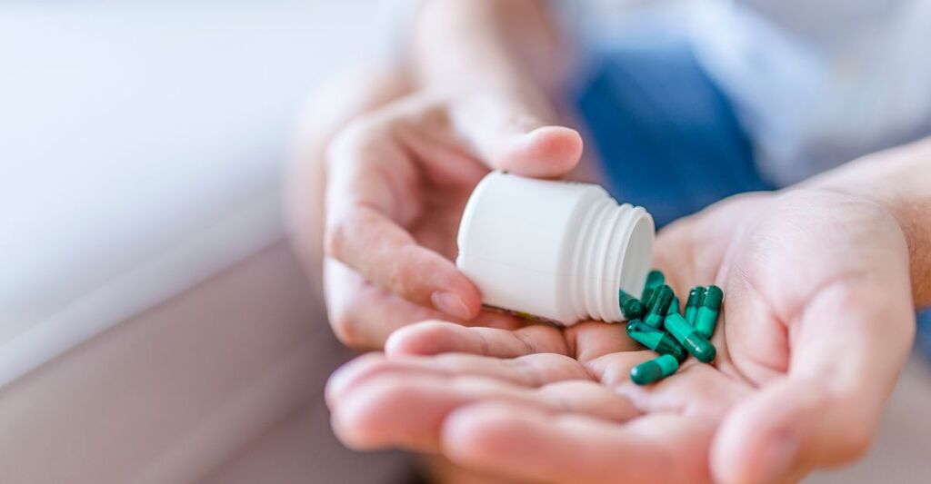 Primo piano di una persona che versa delle capsule verdi da un flacone bianco sul palmo della mano