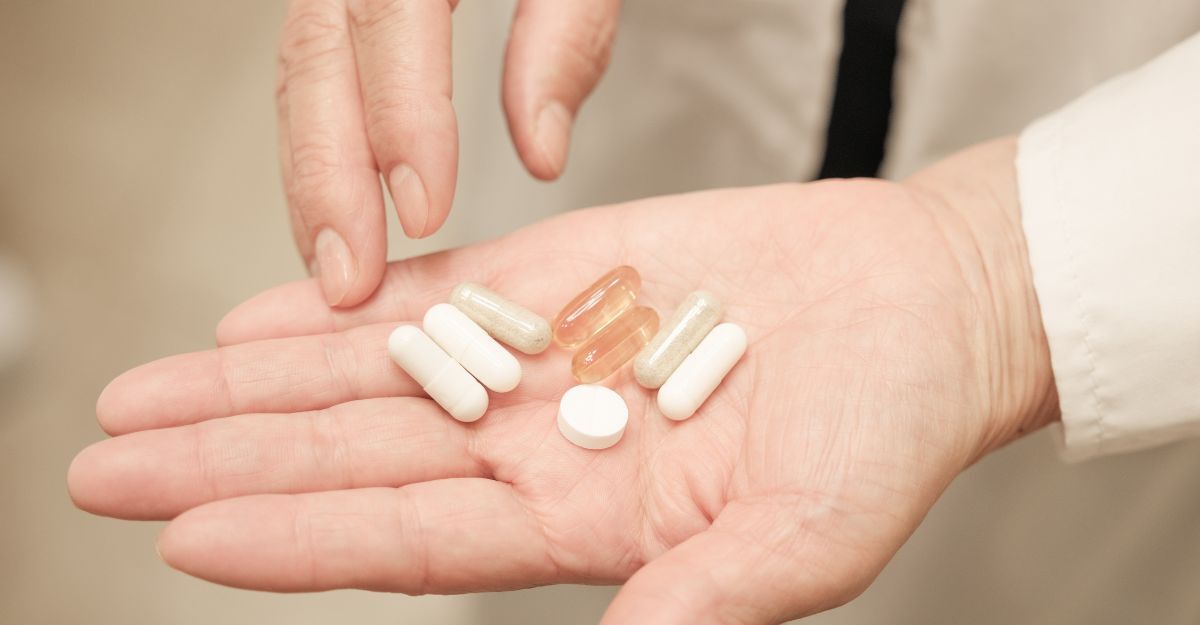 Primo piano di un palmo aperto che contiene diverse pillole, tra cui compresse bianche e capsule trasparenti