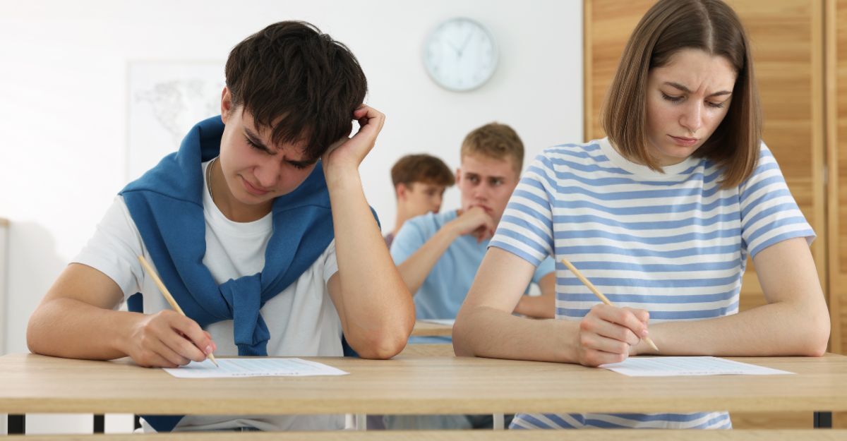 Studenti seduti ai banchi durante un test, con espressioni concentrate e stressate