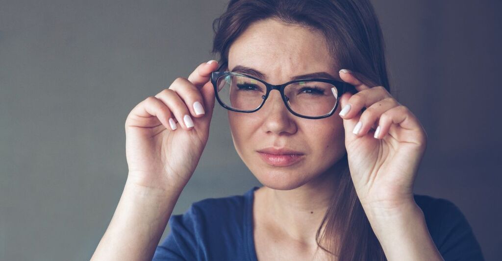 Primo piano di una donna che si sistema gli occhiali sul viso con un'espressione affaticata o dubbiosa