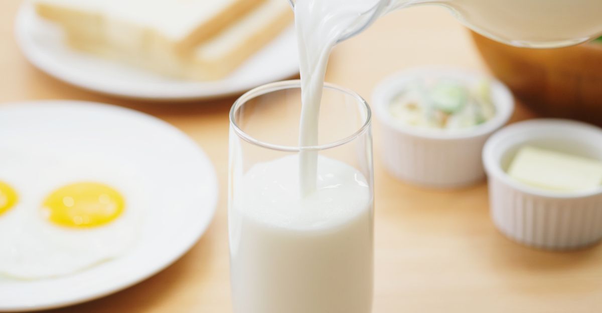 Latte fresco versato in un bicchiere durante una colazione con uova e pane tostato