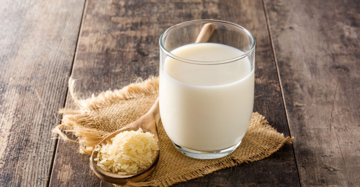 Un bicchiere di latte di riso accanto a un cucchiaio di legno colmo di chicchi di riso su un tavolo rustico