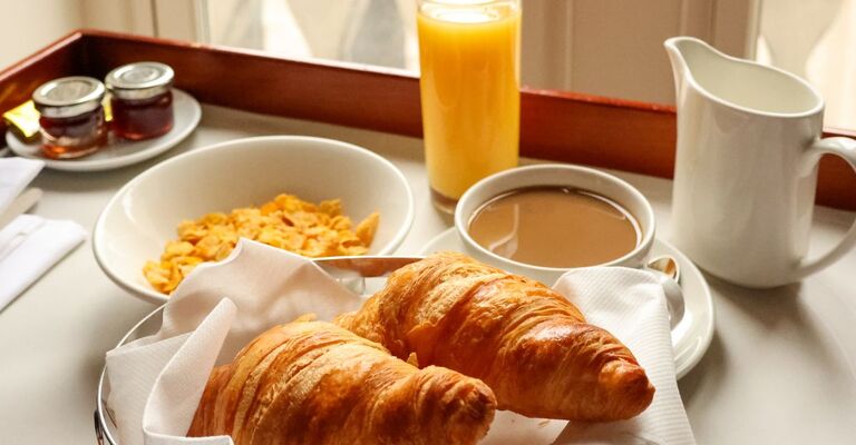 Colazione continentale con cornetti caldi, una ciotola di cereali, succo d'arancia e caffè serviti su un vassoio