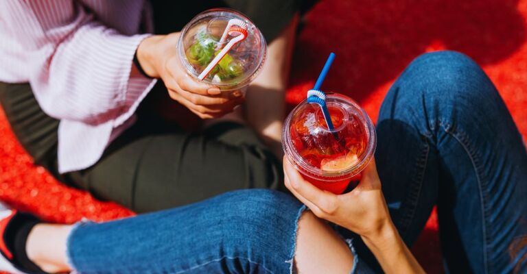 Due ragazze adolescenti sedute a terra in posizione di rilassamento, mentre bevono bibite analcoliche