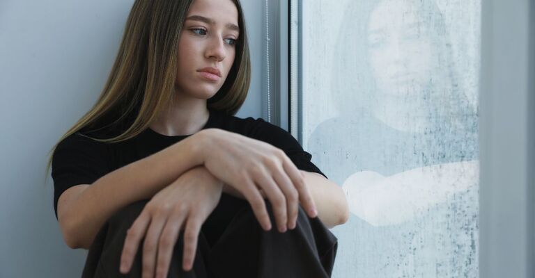 Una ragazza triste che guarda fuori dalla finestra