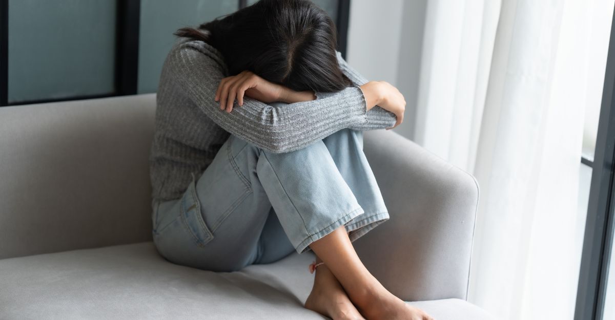 Una ragazza triste seduta sul divano con la testa tra le gambe