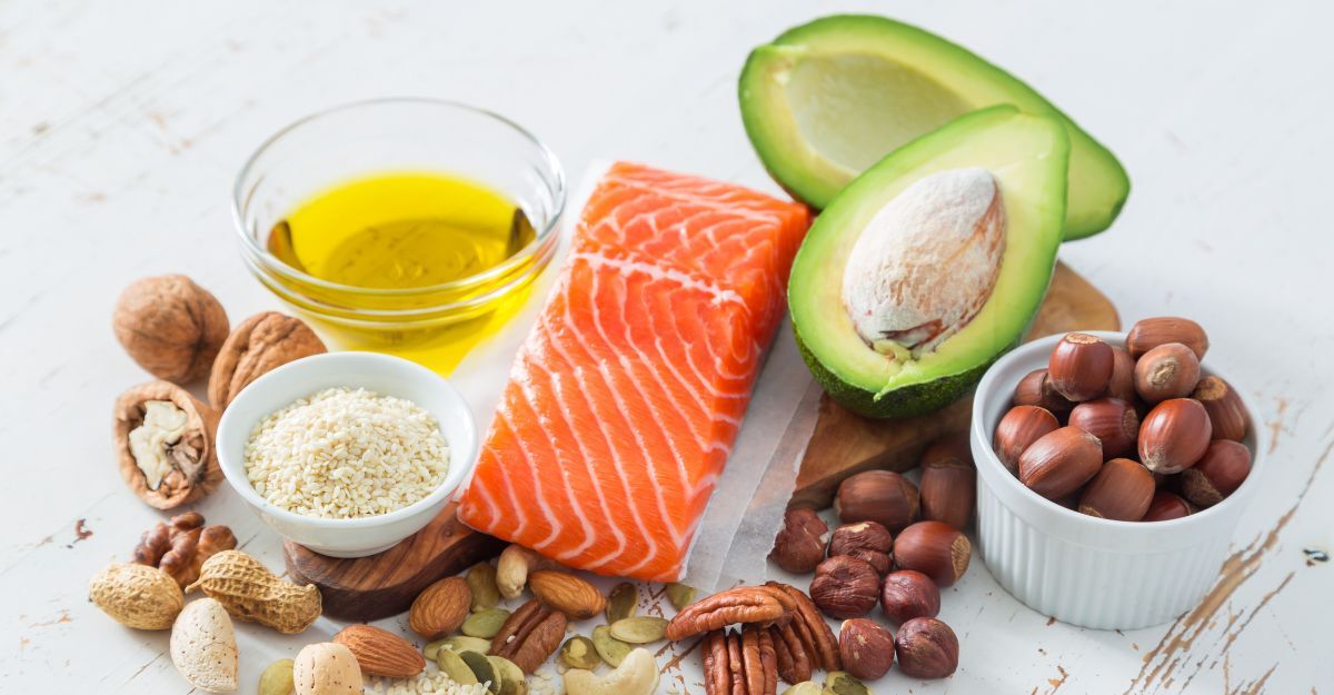 Varietà di alimenti ricchi di grassi sani: salmone crudo, avocado, olio d'oliva, noci e nocciole su fondo bianco